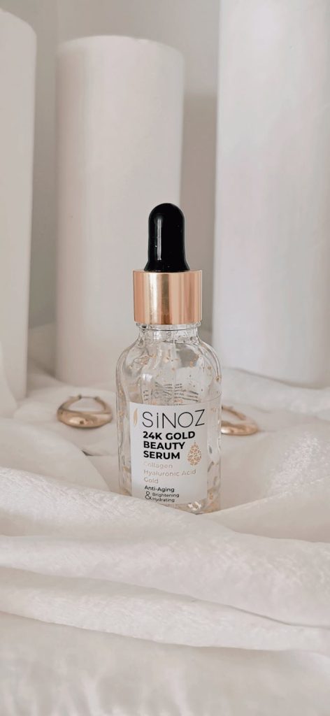 Elegant shot of Sinoz 24k Gold Beauty Serum bottle on white fabric, highlighting luxury skincare.