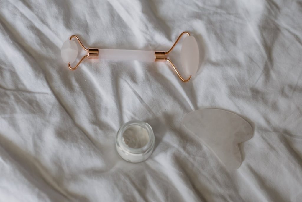 A flat lay of a jade roller, gua sha, and cream on a white sheet conveys a serene skincare ritual.